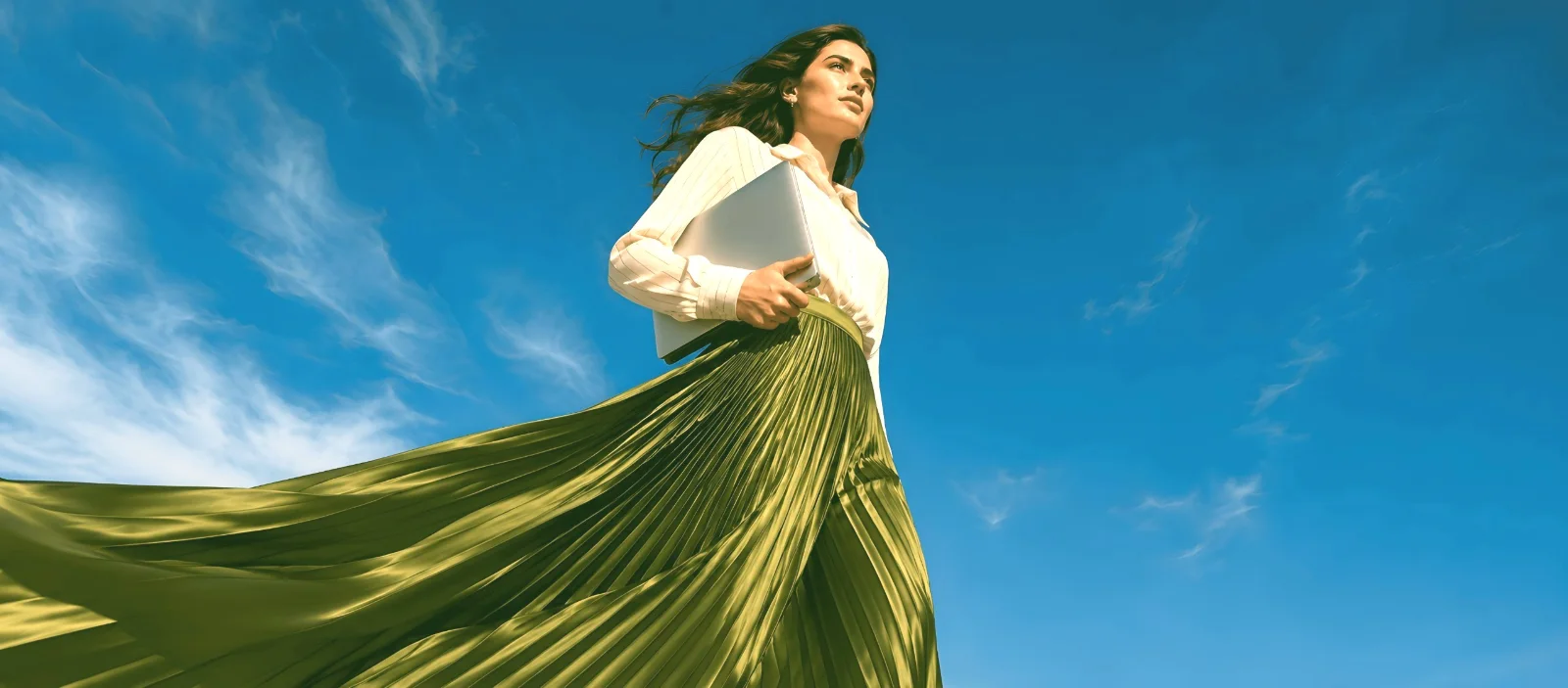 A woman holding a laptop against a clear blue sky